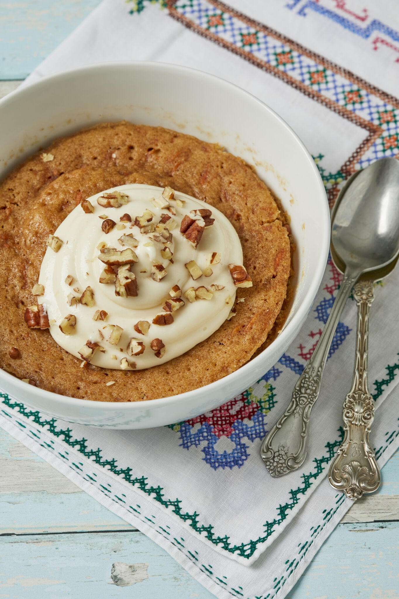 Soft moist carrot cake in a bowl topped with cream cheese frosting and toasted nuts. 