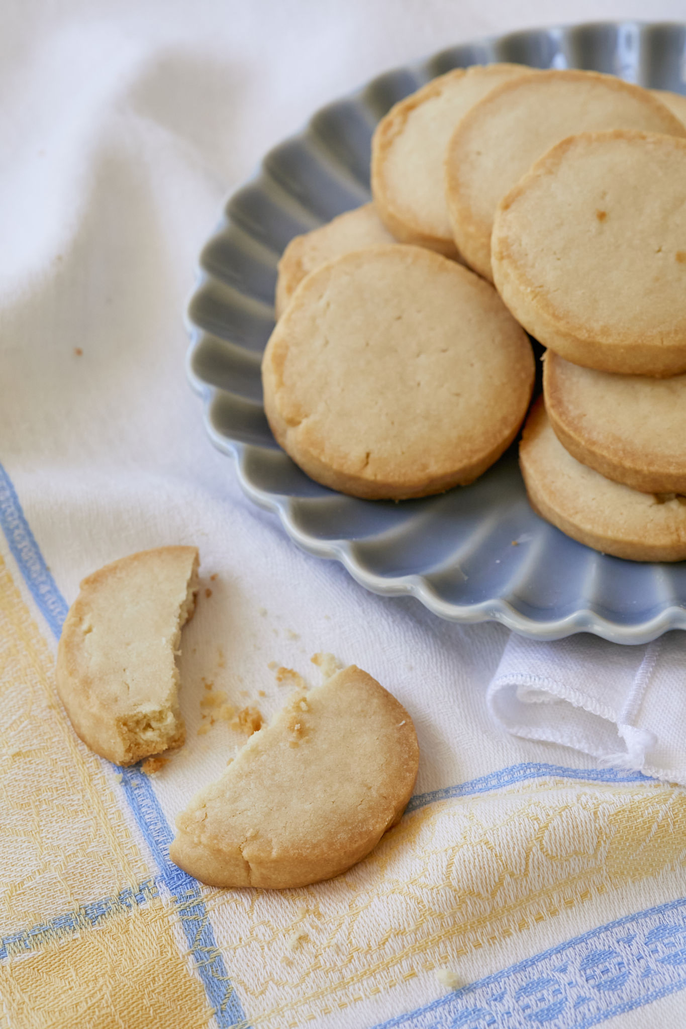 Homemade shortbread cookies are served on a blue dish. One 3 ingredient shortbread cookie is snapped in half, showing how a crispy cookie.