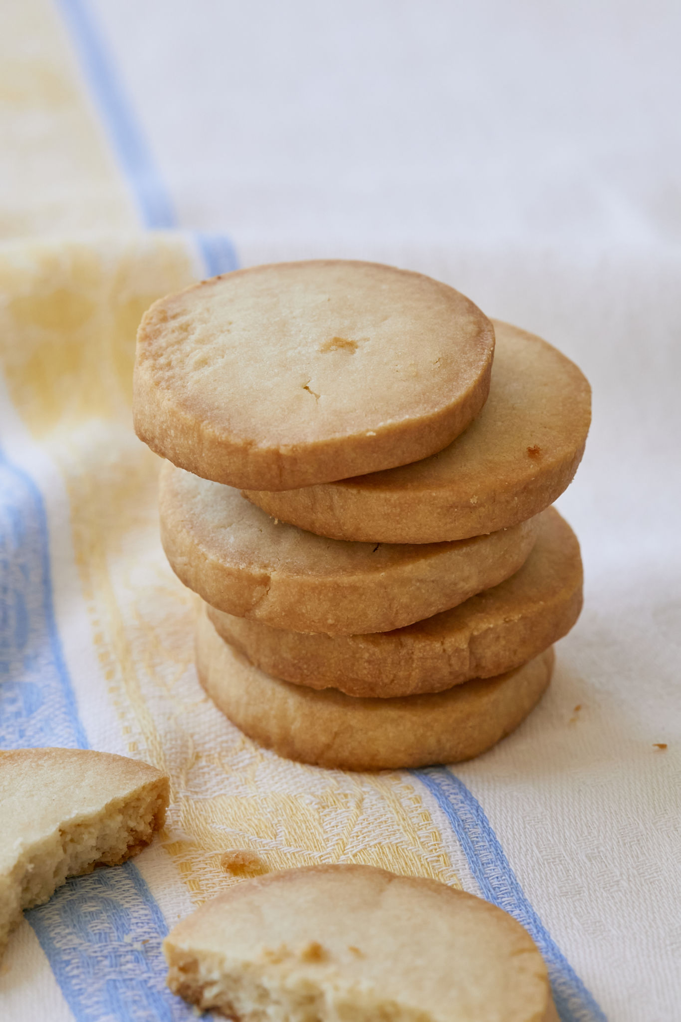Shortbread cookies are stacked on top of each other. One shortbread cookie is broken in half and looks crispy.