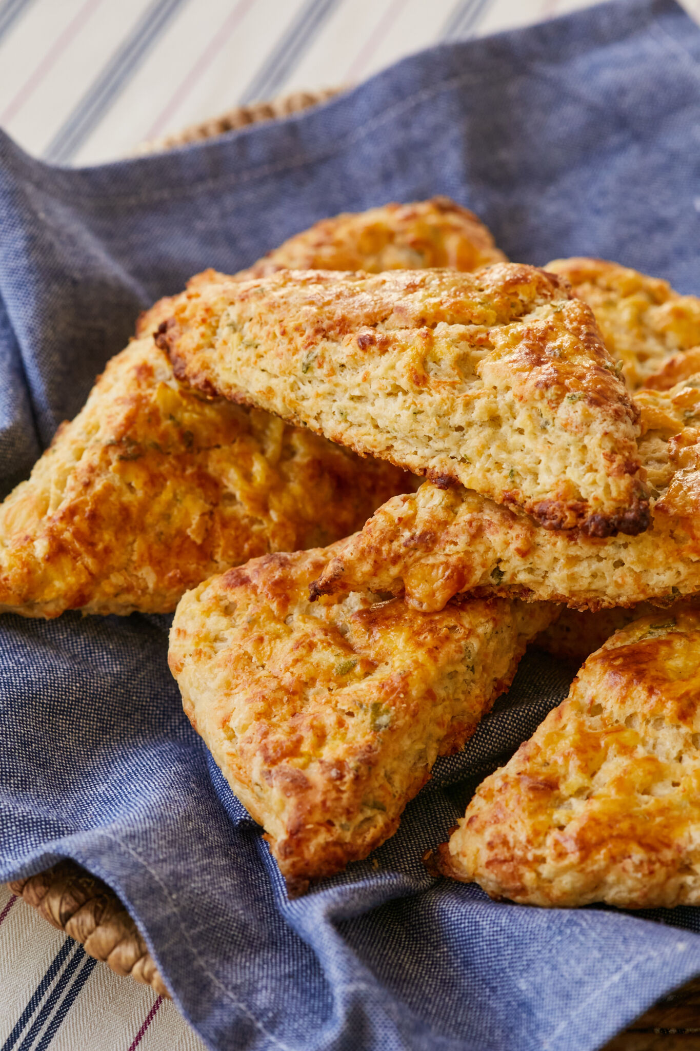 Apple Sage and Cheddar Scones are placed on a blue towel in a basket. They are baked to perfection with gorgeous golden brown color and crispy exterior all around with a crumbly soft interior. 