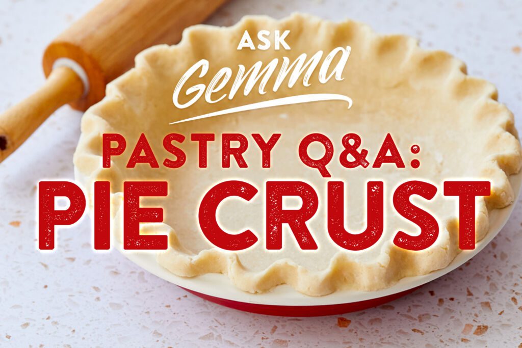 Ask Gemma-Pastry Q&A Pie Crust Questions Answered: a close shot at a buttery, fluted-edge pie crust with smooth exterior, in a red ceramic pan pan. A wooden rolling pin is on the side.