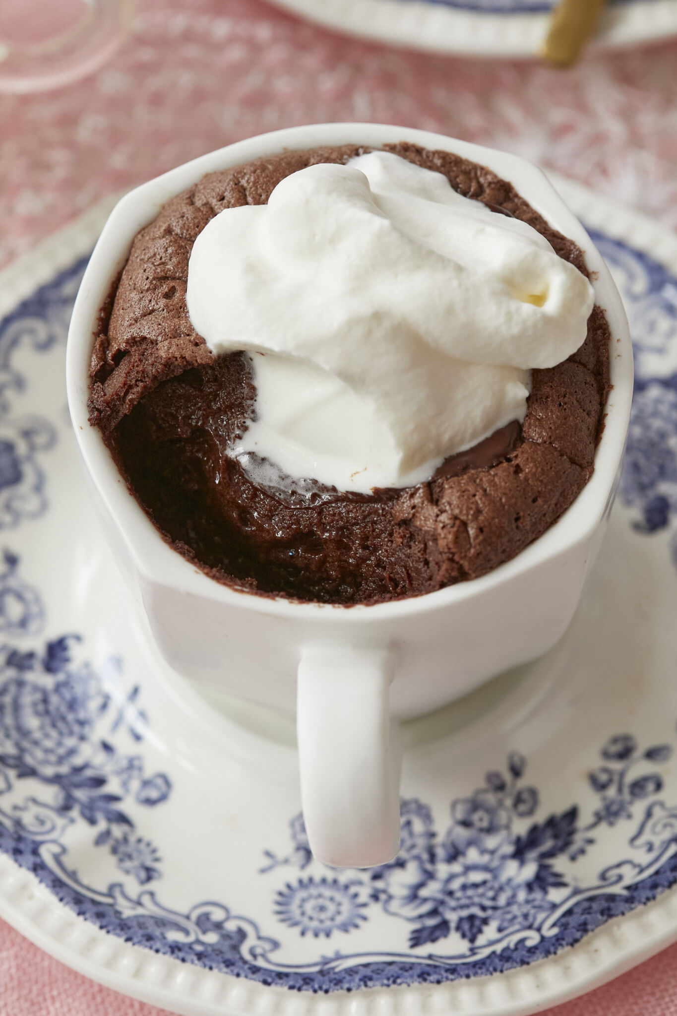 A close shot at baked hot chocolate that has one bite taken shows the gooey center and lightly crispy edge. It's paired with softly whipped cream. 