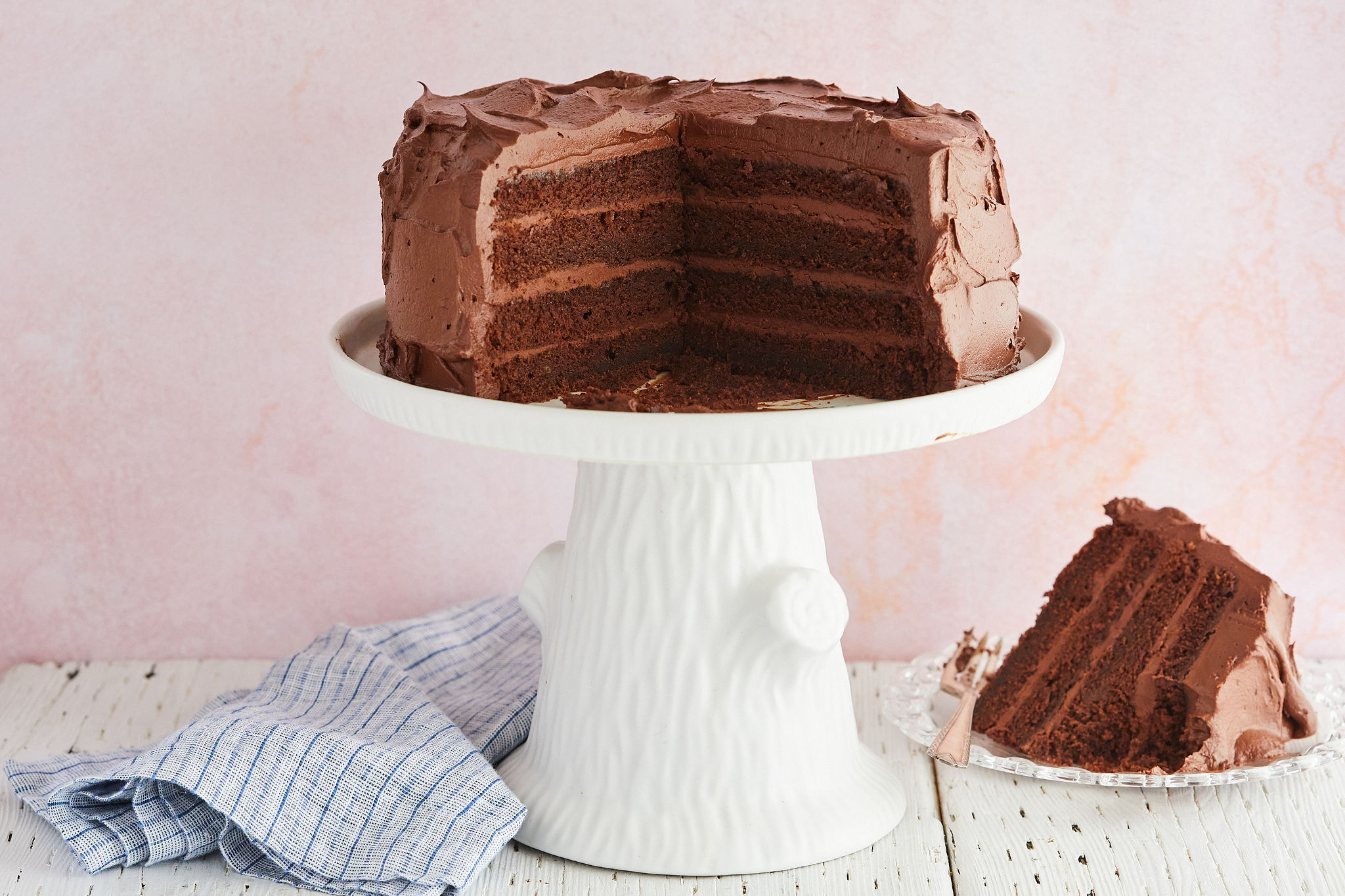 My Best-Ever Chocolate Cake recipe with whipped dark chocolate ganache frosting on a cake stand with a slice removed.