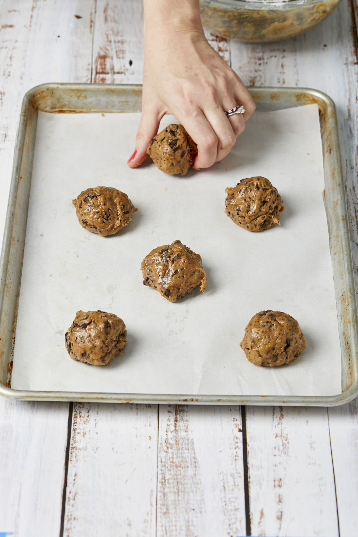 Before baking, placing scooped cookie dough balls 2-3 inches apart on the parchment-lined baking tray. 
