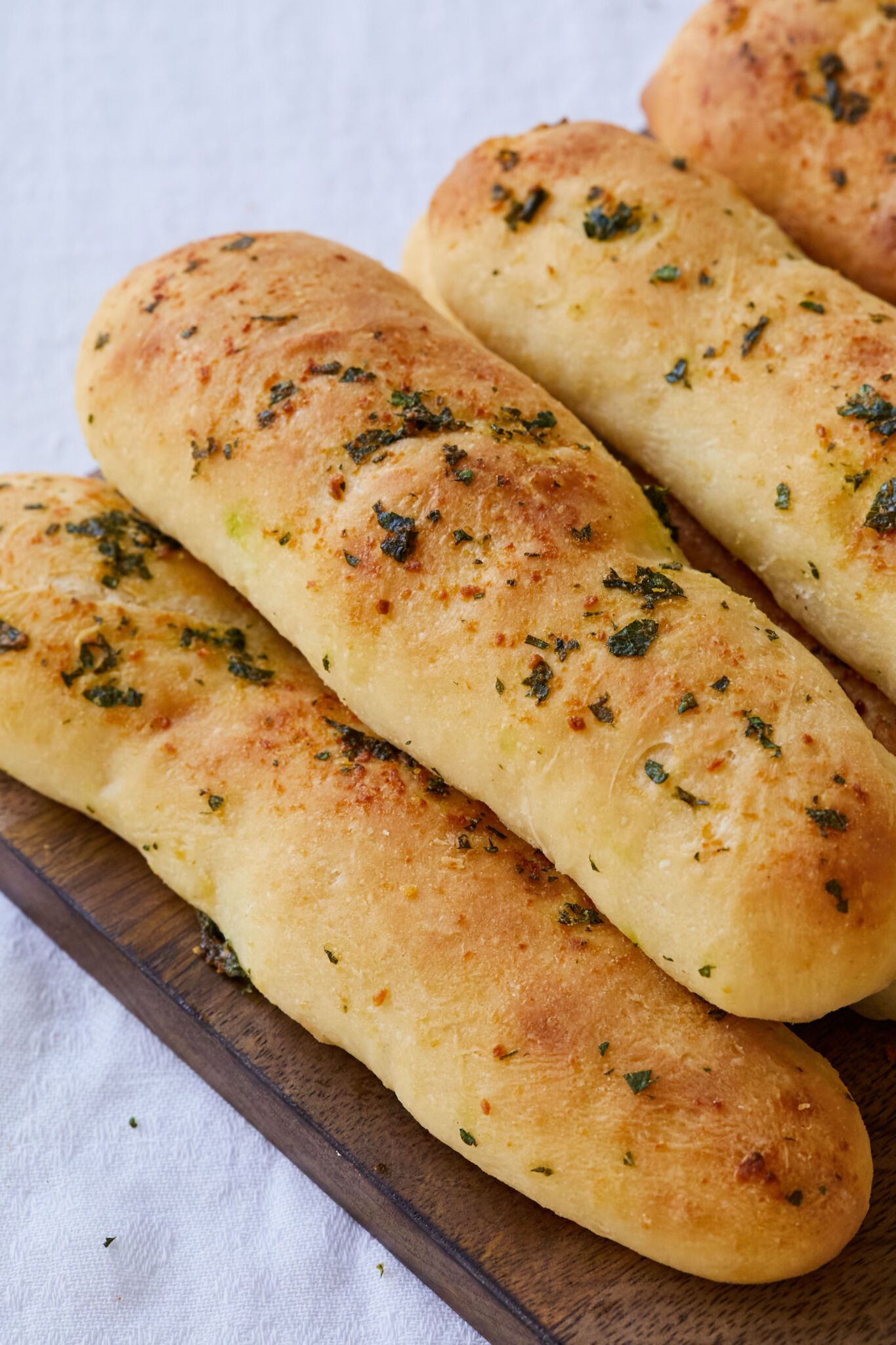 Garlic Breadsticks are shaped into long, thin rods and were baked until golden brown. The exterior looks slightly crispy with brushed butter, garlic and herbs. 