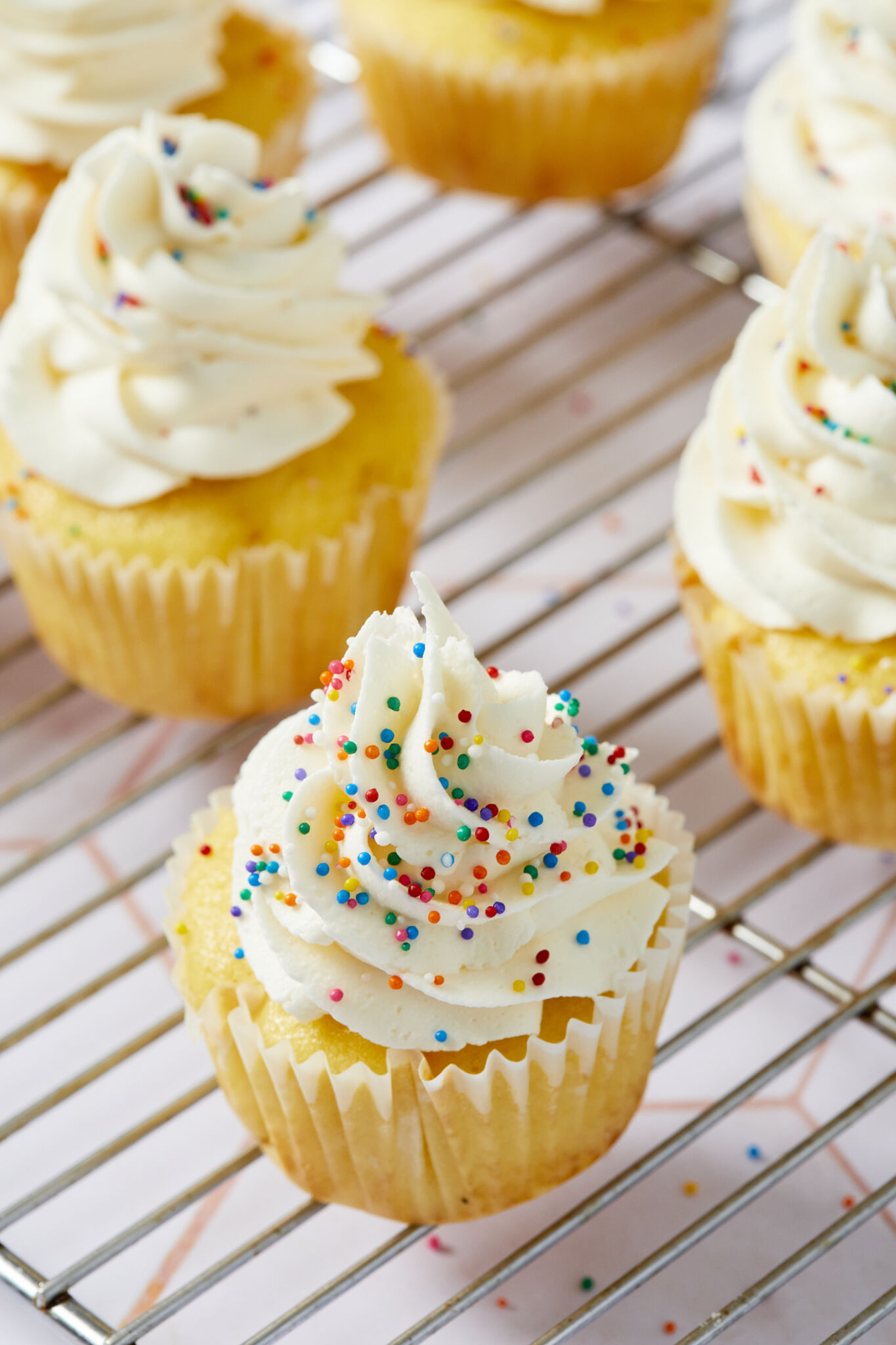 Best-Ever Buttercream Frosting decorated vanilla cupcakes topped with rainbow color sprinkles. 