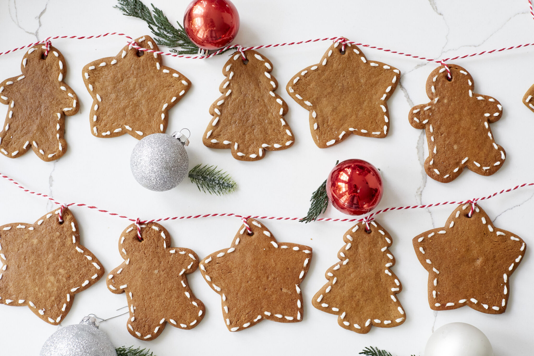 Gingerbread Cookies are baked until brown and iced with white icing on the edges. They're strung together with a red-white twine.