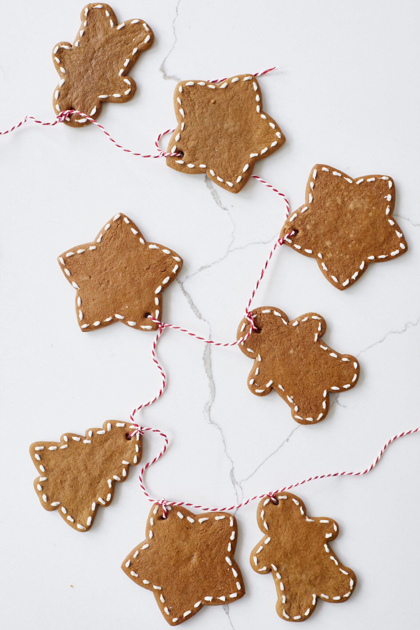 Gingerbread Cookies are baked until brown and iced with white icing on the edges. They're strung together with a red-white twine.