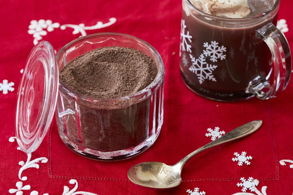 Homemade Hot Chocolate Mix in a glass jar. A mug of hot chocolate made from this is next to it with whipped cream on top.