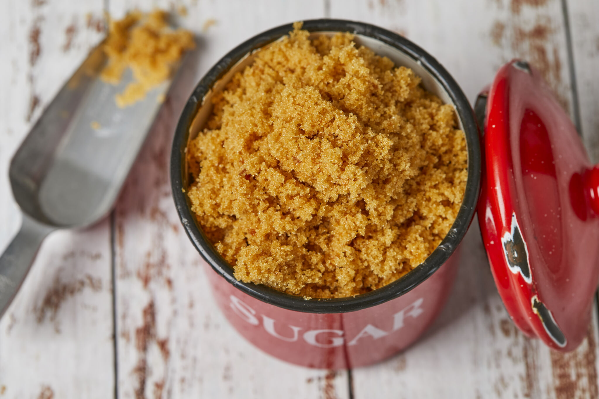 Homemade Brown Sugar is golden brown and moist, stored in a red enamel mug with a metal scoop on the side in the top left corner.