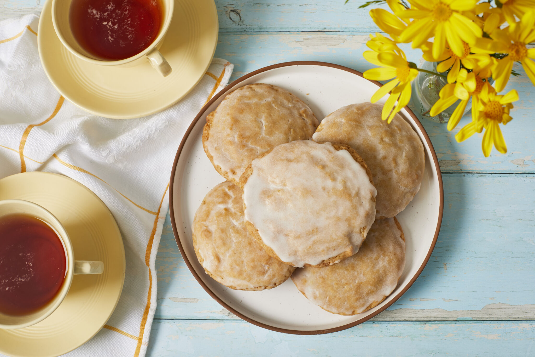 Baked Soft Lemon Cookies dipped with Zesty Lemon Glaze, served on a plate with tea on the side.