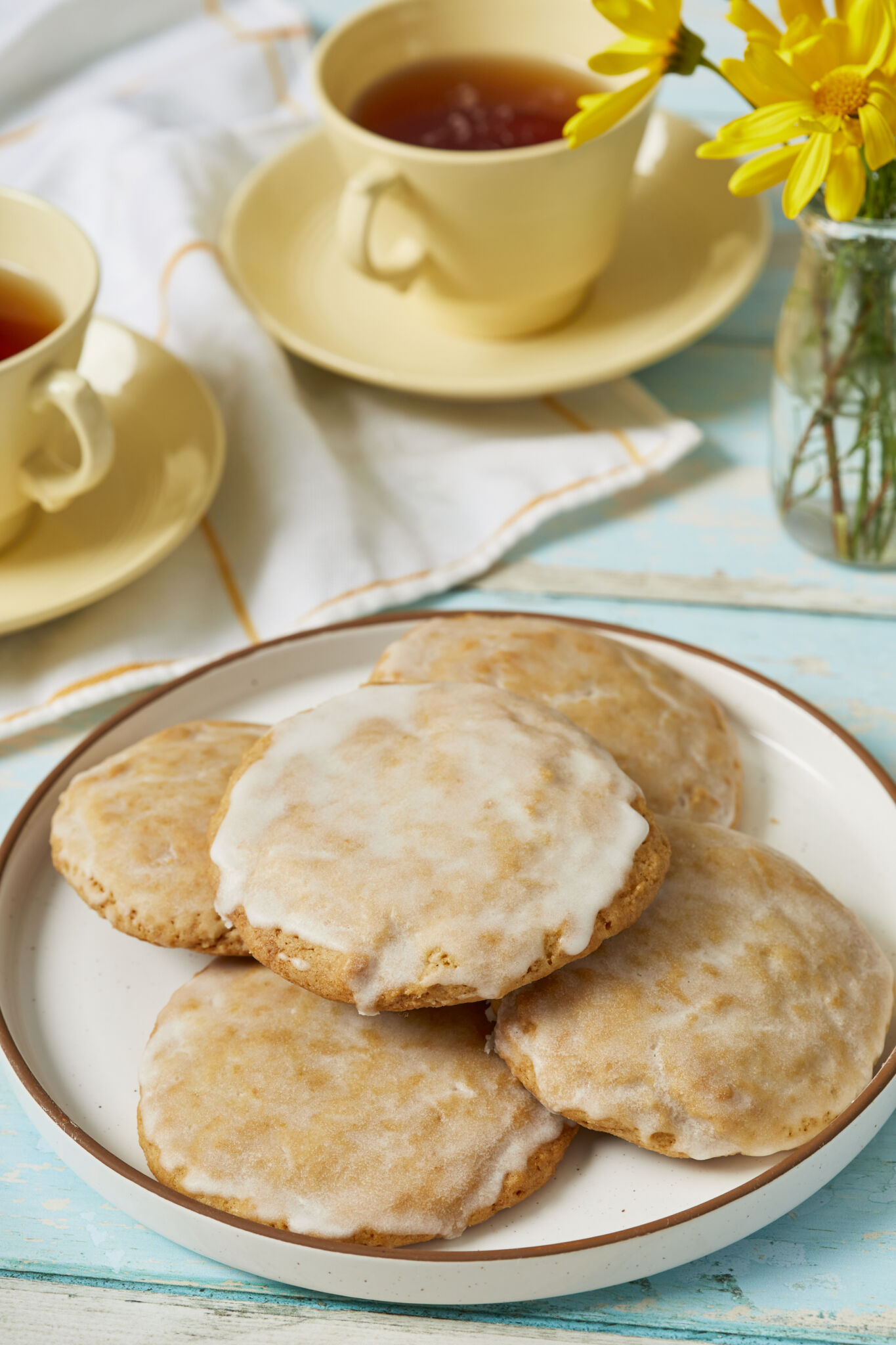 Baked Soft Lemon Cookies dipped with Zesty Lemon Glaze, served on a plate with tea on the side. 