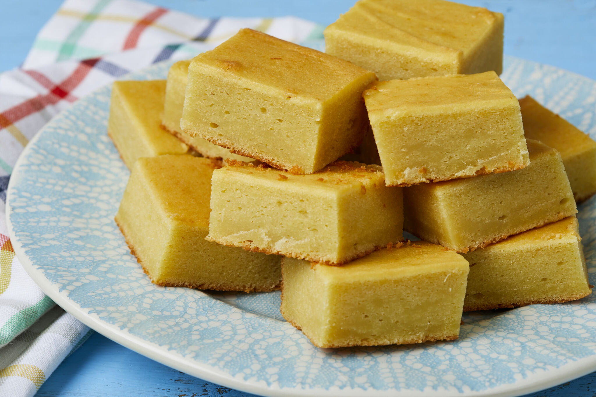 Golden luscious Mango Butter Mochi is piled on a light teal-blue plate, with silky soft texture on top and crispy crust at the bottom.