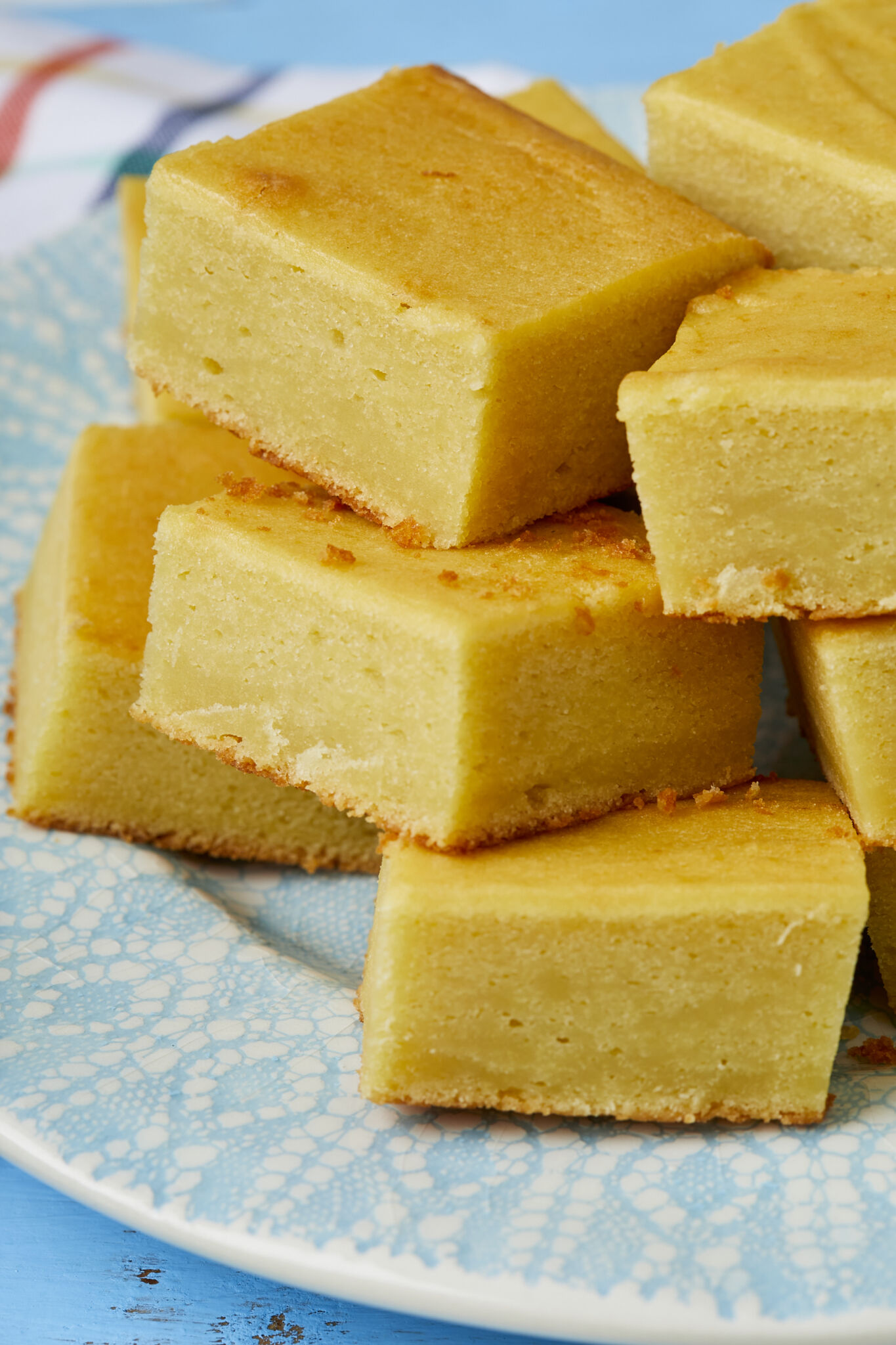Golden luscious Mango Butter Mochi is piled on a light teal-blue plate, with silky soft texture on top and crispy crust at the bottom.