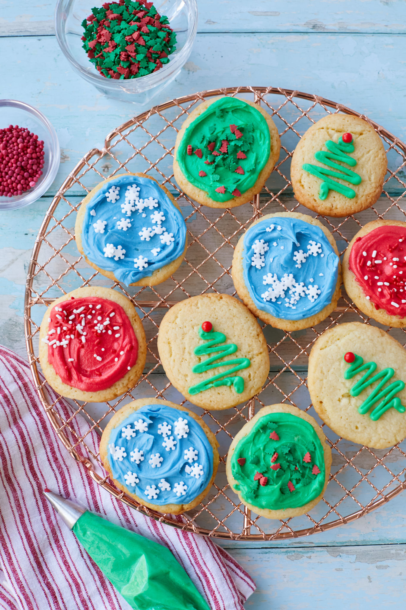 A cooling rack with holiday decorated soft sugar cookies next to sprinkles.