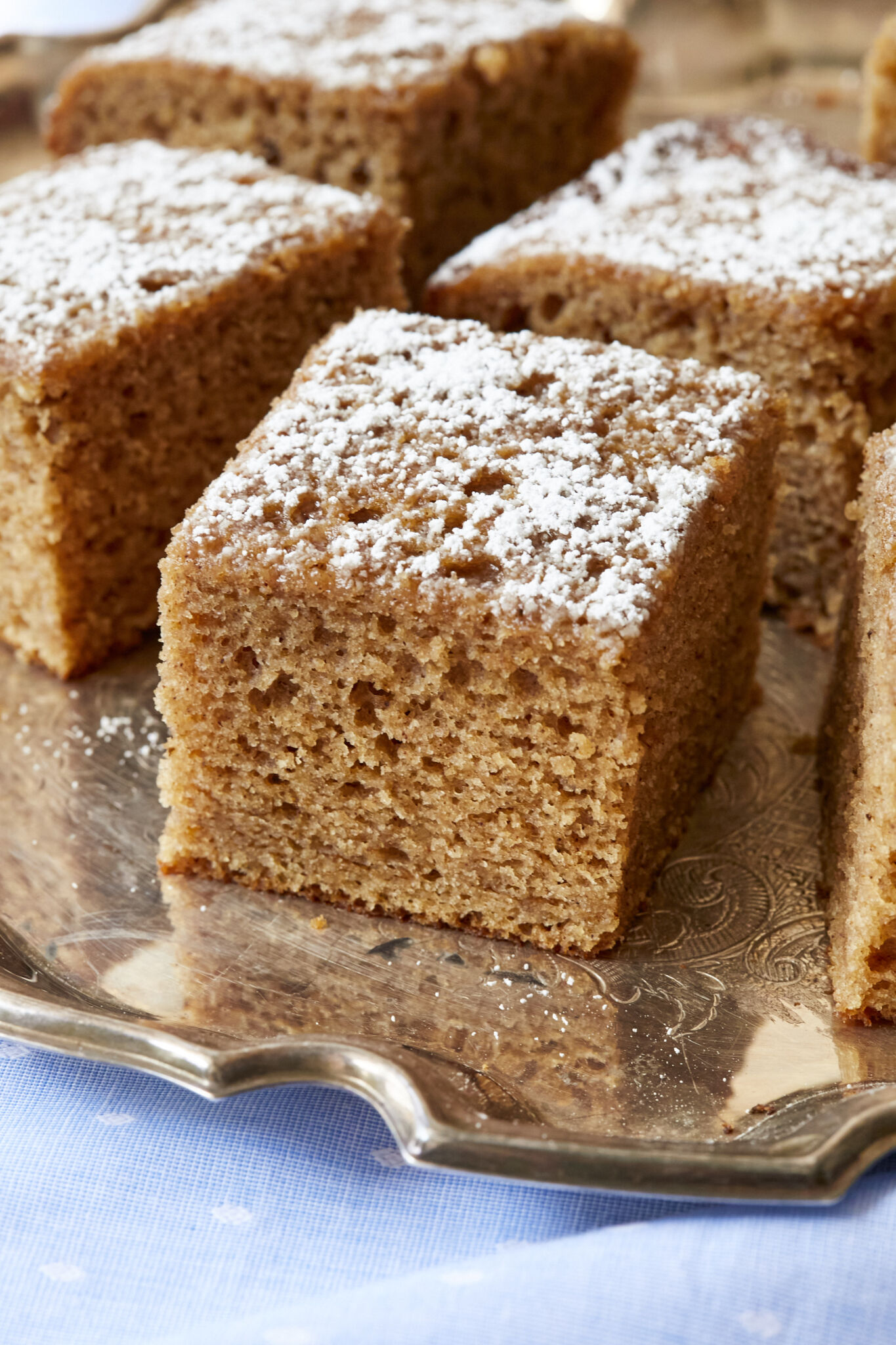 A Traditional Irish Spice Cake is cut into generous squares and served on a silver platter. They have delectably moist, fine crumb and are dusted with powdered sugar.
